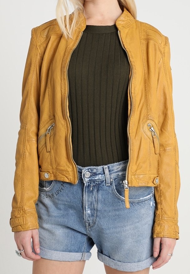 Gul läderjacka med en skräddarsydd design, dragkedjefickor och strukturerade detaljer, kombinerad med en olivgrön ribbad tröja och jeansshorts.