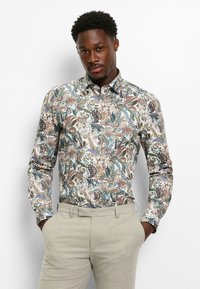 Long-sleeved shirt featuring a floral and paisley pattern in multi-colored tones, made of lightweight fabric, paired with beige trousers.