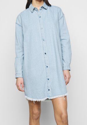 Vaaleansininen denim-paita mekko, jossa on pitkät hihat, napitettava etu ja rispaantunut helma. Siinä on terävä kaulus ja rento istuvuus.