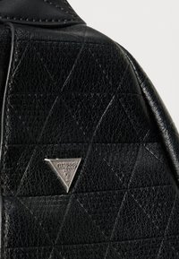 Czarna, teksturowana skórzana torba z diamentowym wzorem oraz wytłoczonym srebrnym trójkątnym logo z nazwą marki.
