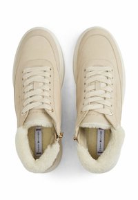 Baskets montantes beiges avec doublure en peluche, laçage à l'avant et accents en métal doré. Dessus en cuir suédé lisse avec un col texturé et duveteux.