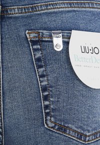 Jeans in denim blu con dettaglio in metallo argentato sulla tasca posteriore. L'etichetta attaccata mostra il marchio "LIU JO" e "Better Denim".
