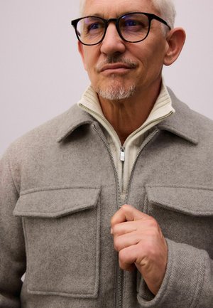 Chaqueta de mezcla de lana gris con cierre de cremallera, dos bolsillos en el pecho y un cuello plano. El interior cuenta con una capa de punto en color crema.