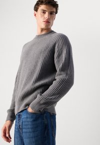 Gray ribbed sweater made of knit fabric, featuring long sleeves, a round neckline, and a fitted hem, paired with blue jeans.