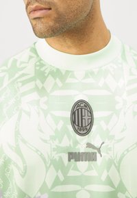 Camiseta deportiva verde claro con un patrón texturizado, presenta el logo del AC Milan y la marca Puma en plata, con cuello redondo y mangas cortas.