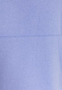 Tejido de sudadera de color púrpura claro con una textura suave, que presenta un acabado liso y ligeramente cepillado, y costuras sutiles. No se aprecian detalles adicionales.