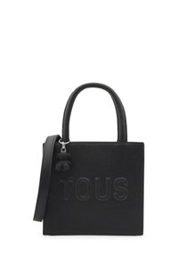 Czarna torebka z teksturowanego materiału, z krótkimi uchwytami, odpinanym paskiem na ramię i akcentem w postaci zawieszki. Wyraźnie widoczny logo "TOUS".