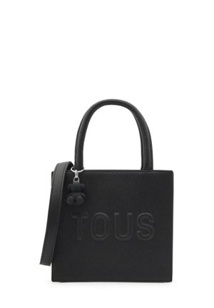 Borsa nera in materiale testurizzato, con manici corti, una tracolla staccabile e un charm decorativo. Logo "TOUS" mostrato in modo prominente.