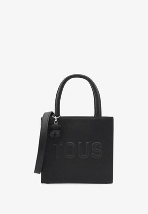Sac à main noir en matériau texturé, avec de courtes poignées, une bandoulière amovible et un accent de charm. Logo "TOUS" affiché de manière proéminente.