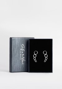 Silveröronhängena har en kaskaddesign med cirkulära former. De presenteras i en mörk sammetstoppad smyckeslåda med en strukturerad grå yta.