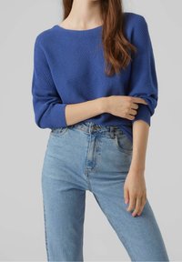 Pull bleu côtelé avec un large col et des manches légèrement retroussées, associé à un jean taille haute bleu clair. Design simple et décontracté.