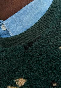 Pull en laine bouclée vert foncé, avec une surface texturée, doté d'un col en denim bleu clair et d'un encolure côtelée verte.