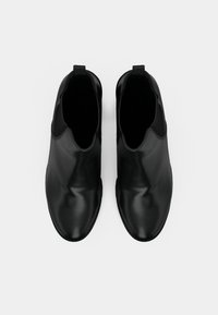 Par de botines de cuero negro sin cordones, con paneles laterales elásticos y tiradores, vistos desde arriba sobre un fondo blanco.