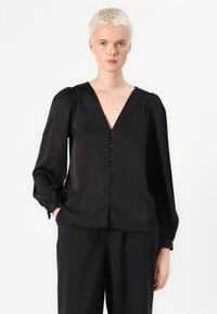 Blusa negra de tela suave, con escote en V, botones frontales y mangas largas abullonadas con detalles en los puños.
