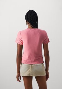 Rosa geripptes Oberteil mit kurzen Ärmeln und gewelltem Saum, das ein figurbetontes Design und weichen Stoff aufweist. Kombiniert mit einem hellen Rock.
