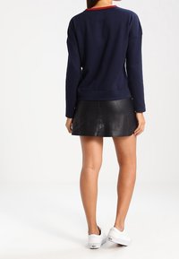 Suéter de manga larga navy con cuello redondo rojo, combinado con una minifalda de cuero negra. Zapatillas blancas completan el conjunto.