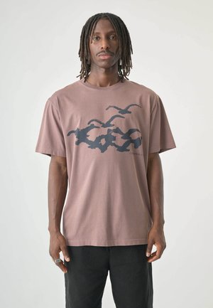 Brown cotton t-shirt features a graphic design of birds in dark blue. It has short sleeves and a crew neckline.
