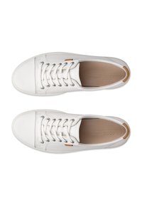 Vista dall'alto di sneakers bianche basse con lacci bianchi, suole interne color cuoio e piccoli tiranti marroni sul tallone.