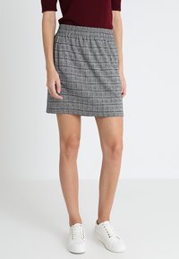 Falda de cuadros grises con cintura elástica. Largo corto, textura suave, combinada con zapatillas blancas.