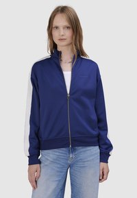 Granatowa kurtka sportowa na zamek z białymi panelami bocznymi, żebrowanymi mankietami i kołnierzem. Wykonana z miękkiego materiału, z delikatnym logo na klatce piersiowej.