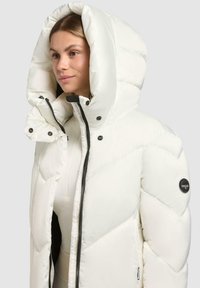 Witte pufferjack met een grote capuchon, zwarte rits en accenten, voorzien van een doorgestikt ontwerp en een logo op de linkermouw.