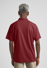 Polo shirt met korte mouwen in donkerrood met een gestructureerde stof, een platte kraag en zijslitsen voor meer bewegingsgemak.