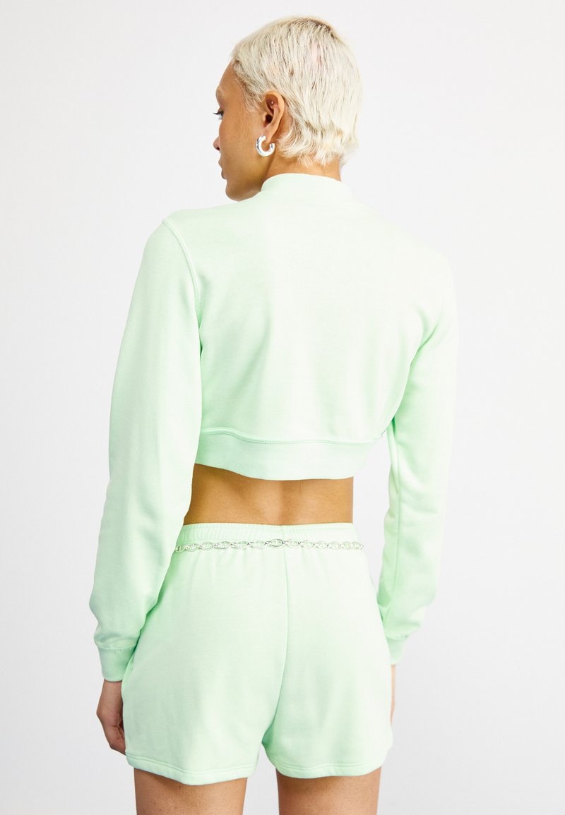 Sudadera corta de color verde menta con mangas largas, combinada con pantalones cortos a juego que presentan un dobladillo decorativo en la cintura. Material de algodón suave.