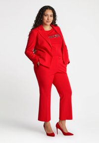 Czerwona dopasowana marynarka i pasujące, krótkie spodnie z gładkiego materiału, zestawione z czerwoną koszulką z designem z cyrkonii. Czerwone szpilki.