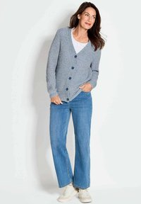 Hellblauer Strickcardigan mit V-Ausschnitt, Knopfverschluss und gerippter Textur, kombiniert mit schmal geschnittenen Jeans und weißen Sneakern.