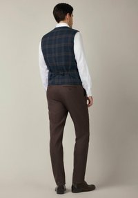 Granatowa kamizelka w kratę z dopasowanym tyłem i regulowanym zapięciem, noszona na białej koszuli, w zestawie z brązowymi spodniami garniturowymi i butami.