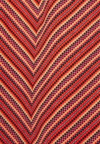 Tissu multicolore avec un motif en zigzag rouge, orange, noir et crème. Présente des points et des accents floraux dans tout le design.