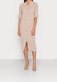 Robe côtelée beige à mi-cuisse avec des manches courtes, fermeture à boutons à l'avant et fente sur le côté. Associée à des talons hauts nus avec des lanières.