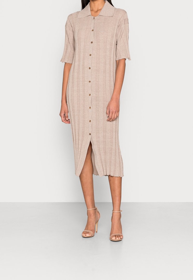 Robe côtelée beige à mi-cuisse avec des manches courtes, fermeture à boutons à l'avant et fente sur le côté. Associée à des talons hauts nus avec des lanières.