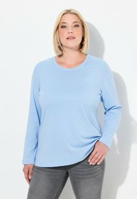 Světle modrá dlouhá rukávová košile vyrobená z měkké látky, s kulatým výstřihem a volným střihem, v kombinaci s tmavě šedými džíny.