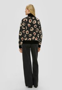 Zwarte trui met luipaardprint in crème en rood, met een zwarte zoom en manchetten. Gekocht met wijde, donkere jeans. Gezicht vanuit de achterkant.