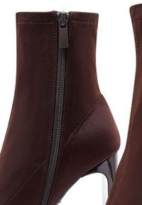 Bottines marron en tissu lisse, avec une fermeture éclaire sur le côté, un bout pointu et un talon haut brillant. Les détails de couture sont visibles.