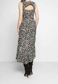 Vestido sin mangas de estampado de leopardo con la espalda descubierta, de longitud midi, fabricado en tela ligera y con un dobladillo con volantes. Llevado con botas negras hasta la rodilla.
