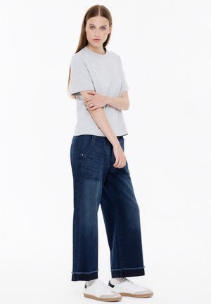 Gray short-sleeve t-shirt paired with dark blue wide-leg jeans featuring front pockets and frayed hem, worn with white sneakers.