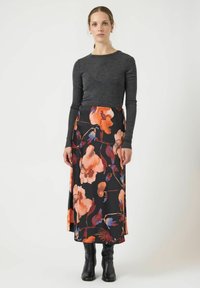 Larga falda negra con un vibrante patrón floral en naranja y púrpura, combinada con una blusa ajustada de manga larga gris. Botas negras hasta la rodilla.