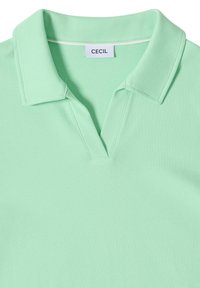Polo verde chiaro con scollo a V, colletto piatto e etichetta bianca con la scritta "CECIL" al collo.