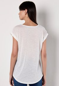 T-shirt blanc à manches courtes en tissu léger et texturé, avec des poignets retroussés et un ourlet arrondi, vu de dos.