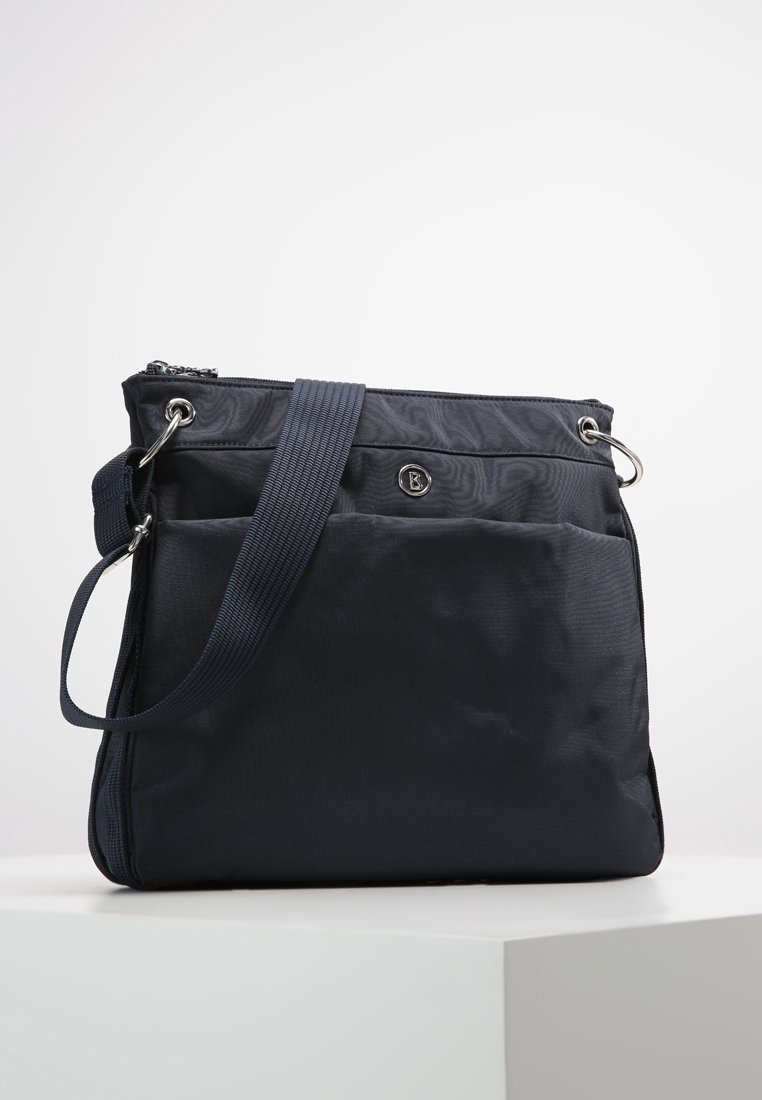 Mörkblå axelväska med justerbar rem, ficka fram, dragkedjestängning och liten rund metalllogotyp på en enfärgad ljus bakgrund.