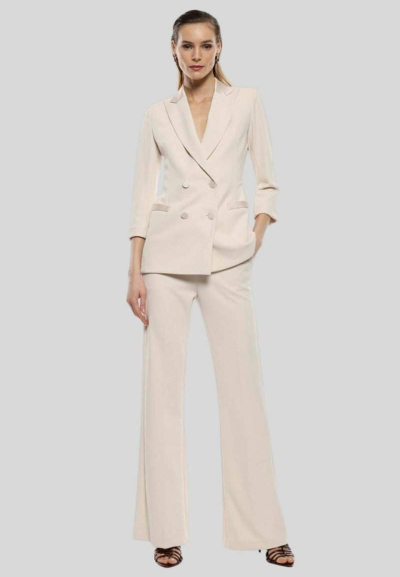 Blazer doppiopetto crema con rever a punte, abbinato a pantaloni a gamba larga. Tessuto morbido, vestibilità sartoriale e tasche frontali.