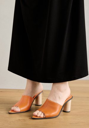 Åpne tå mules i livlig oransje lær med en glatt tekstur, med en blokkhels og et minimalistisk design.