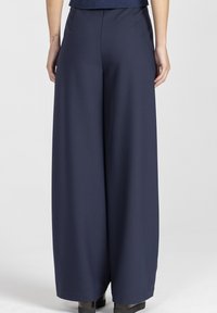 Granatowe spodnie o szerokich nogawkach z gładką fakturą, z wysokim pasem i bocznymi kieszeniami. Nogawki są lekko zwężane przy kostkach.