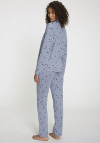 Ljust blå pyjamas-set med lång ärm och byxor, prytt med ett upprepat mönster av små mörka hjärtan. Tillverkad av mjukt tyg, avslappnad passform.