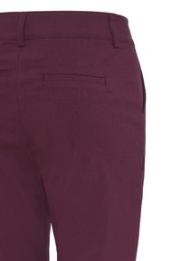 Gros plan sur un pantalon violet foncé montrant une poche arrière avec une fente horizontale et des passants de ceinture à la taille.