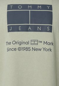 Světle zelená bavlněná košile s námořnickým grafickým designem, který obsahuje text a logo "TOMMY JEANS", a nápis "The Original Mark Since 1985 New York."