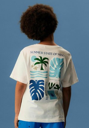 Person with curly hair wearing a white T-shirt with tropical leaf and palm tree prints and text reading "SUMMER STATE OF MIND" on the back.