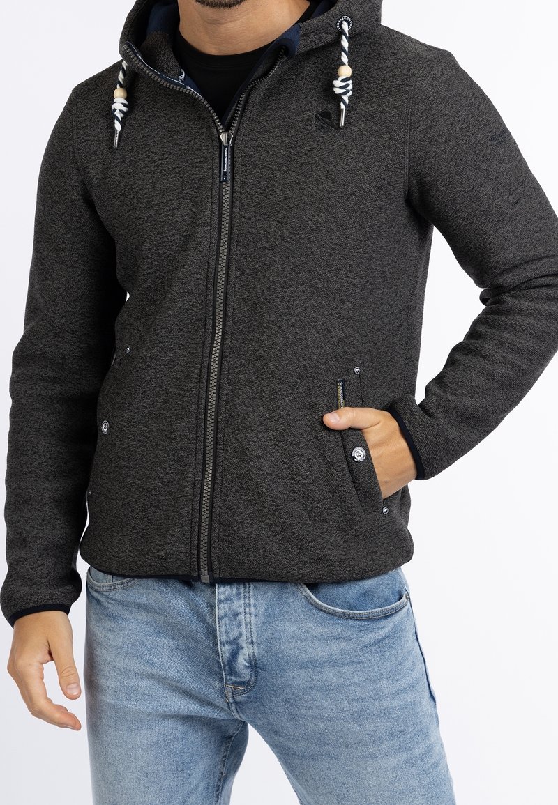 Grå zip-up hoodie med texturerad tyg, justerbar dragsko på huva och två framfickor. Matchat med ljusblå denimjeans.